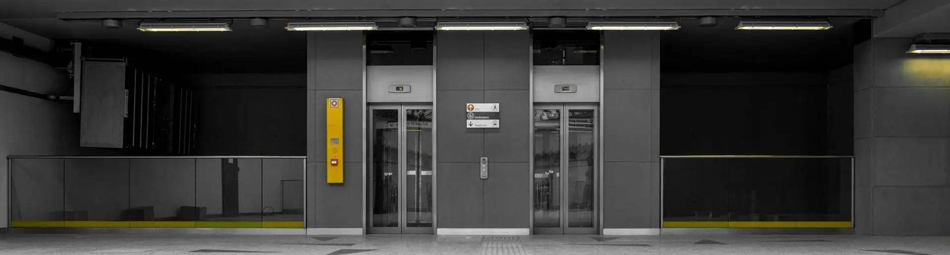 Dos ascensores panorámicos con puertas de vidrio y panel de control amarillo en una estación de transporte público.
